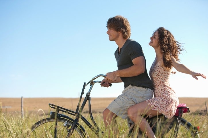 A young couple riding a bike in the fields enjoying life, they are first home buyer and are relaxing now they have the right help.